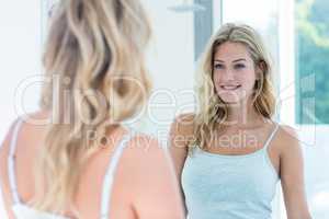Smiling beautiful young woman looking at herself in the bathroom