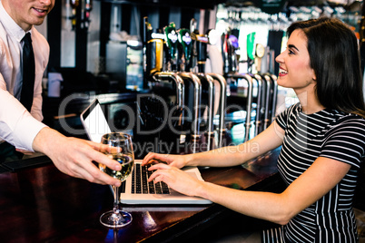 Barman giving a glass of wine at woman using laptop
