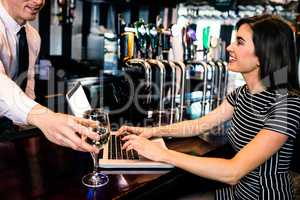 Barman giving a glass of wine at woman using laptop