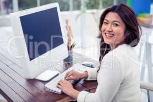 Smiling Asian woman on computer looking back at the camera