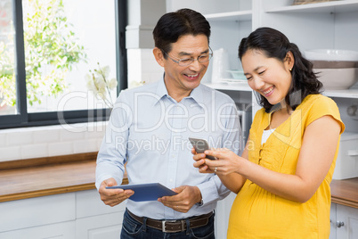 Happy expectant couple using tablet and smartphone