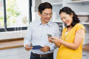 Happy expectant couple using tablet and smartphone