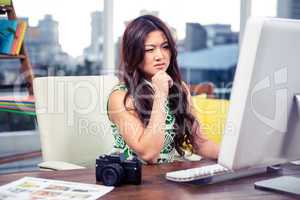 Focused Asian woman using computer with hand on chin