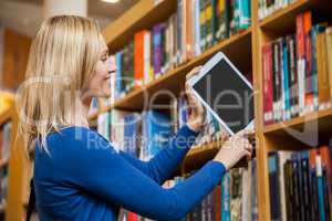 Female student tidying a tablet in a bookshelf