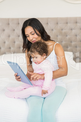 Smiling brunette holding her baby and using tablet