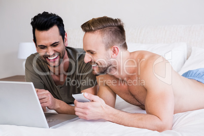 Smiling gay couple using laptop and phone