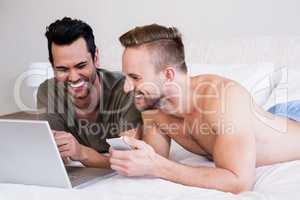 Smiling gay couple using laptop and phone