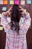 Brunette with hands on hair in front of sticky notes on wooden w