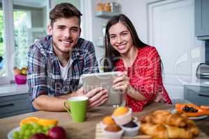 Happy couple having breakfast and using tablet