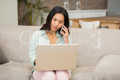 Unsmiling brunette on a phone call using laptop