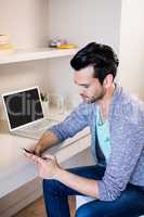 Thoughtful man using smartphone and laptop