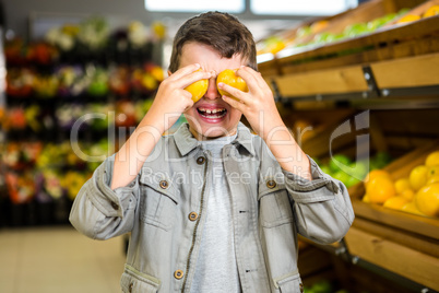 Cute boy covering his eyes with oranges