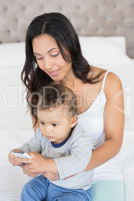 Happy brunette holding her baby and using smartphone