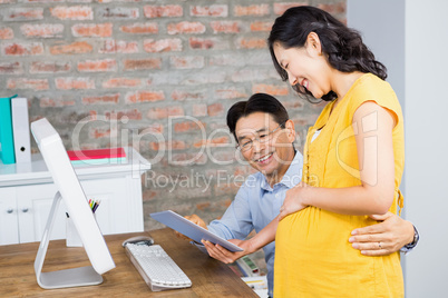 Smiling pregnant woman showing tablet to her husband