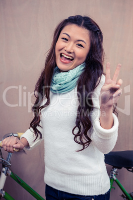 Asian woman holding bike and making peace sign with hand