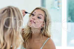 Smiling beautiful young woman putting on mascara in the bathroom