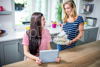 Upset woman showing dirty dishes to friend