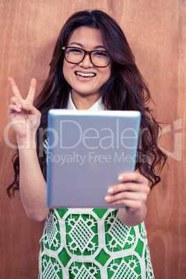 Smiling Asian woman holding tablet and making peace sign with ha