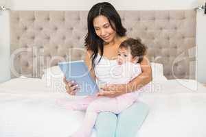Smiling brunette holding her baby and using tablet