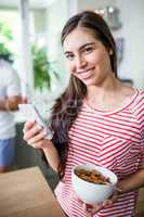 Smiling brunette using smartphone and holding bowl of cereals