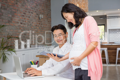 Smiling pregnant woman showing tablet to her husband