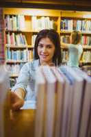 Smiling brunette picking out a book of bookshelves