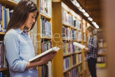 Serious students reading next to bookshelf