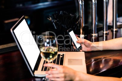 Woman texting and using laptop with wine