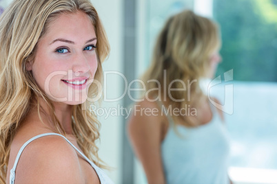 Smiling beautiful young woman looking at herself in the bathroom