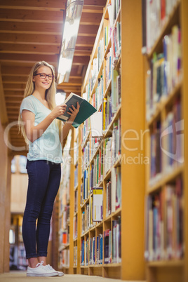 Blonde student reading book next to bookshelf