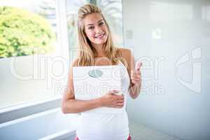 Woman holding a weighting scale with thumbs up