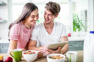 Happy couple using tablet and having breakfast