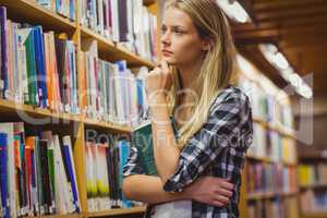 Thoughtful student looking at bookshelf