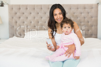 Smiling brunette holding her baby and using smartphone