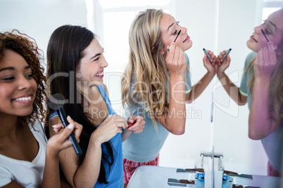 Three smiling friends putting makeup on together