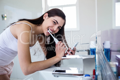 Brunette using smartphone while brushing teeth