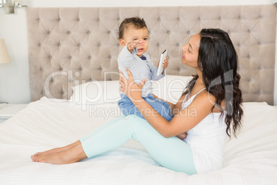 Happy brunette holding her baby who is holding smartphone