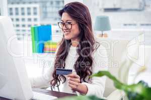 Smiling Asian woman on computer holding credit card