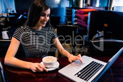 Woman having coffee and using laptop