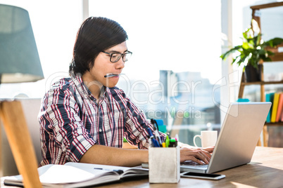 Hipster businessman with pen in mouth using laptop