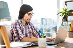 Hipster businessman with pen in mouth using laptop