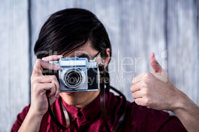 Hipster taking pictures with an old camera while making thumbs u