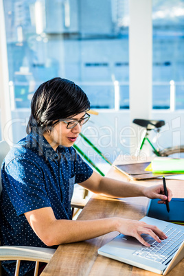 Smiling hipster businessman using laptop and graphic tablet