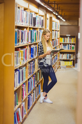 Blonde student reading book next to bookshelf