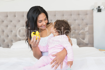 Happy brunette showing yellow duck to her baby