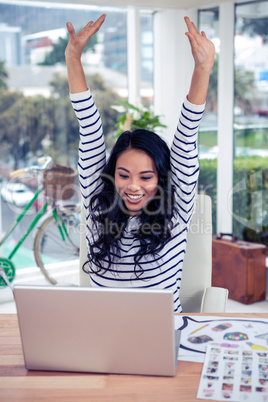 Happy Asian woman with arms raised looking at laptop