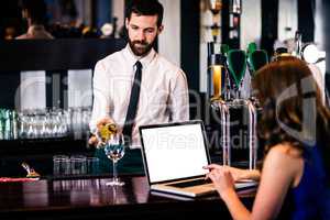 Barman giving a drink to customer using laptop