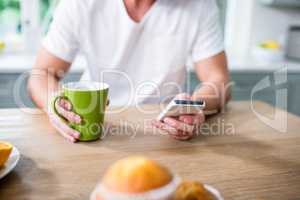 Handsome man using smartphone and holding cup