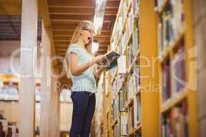 Blonde student reading book next to bookshelf