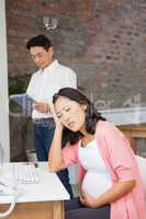 Suffering pregnant woman sitting at desk